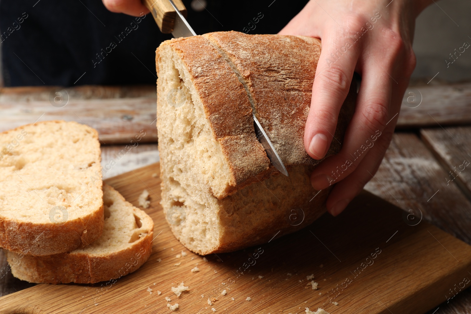 Woman cutting fresh bread at wooden table, closeup Photo of Woman cutting fresh bread at wooden table, closeup