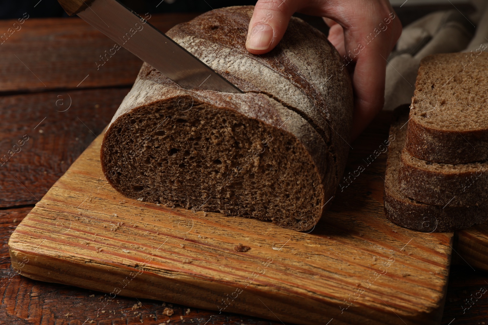 Woman cutting fresh bread at wooden table, closeup Photo of Woman cutting fresh bread at wooden table, closeup