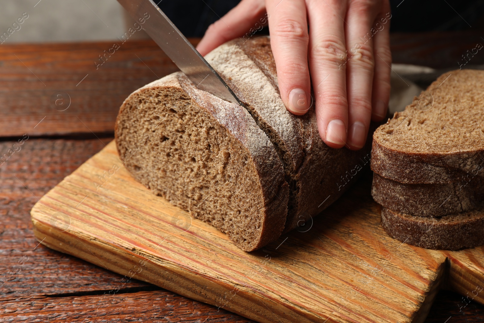 Woman cutting fresh bread at wooden table, closeup Photo of Woman cutting fresh bread at wooden table, closeup