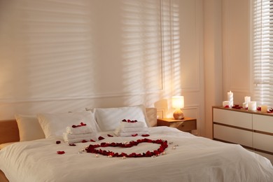 Photo of Heart made with rose petals and burning candles on bed indoors
