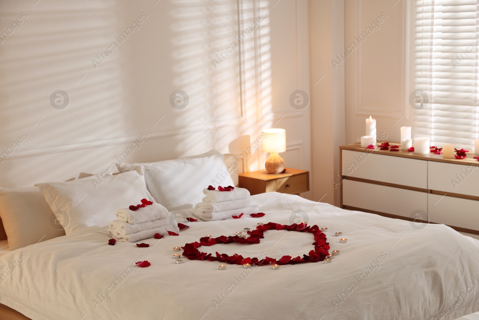 Heart made with rose petals and burning candles on bed indoors Photo of Heart made with rose petals and burning candles on bed indoors