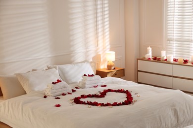 Photo of Heart made with rose petals and burning candles on bed indoors