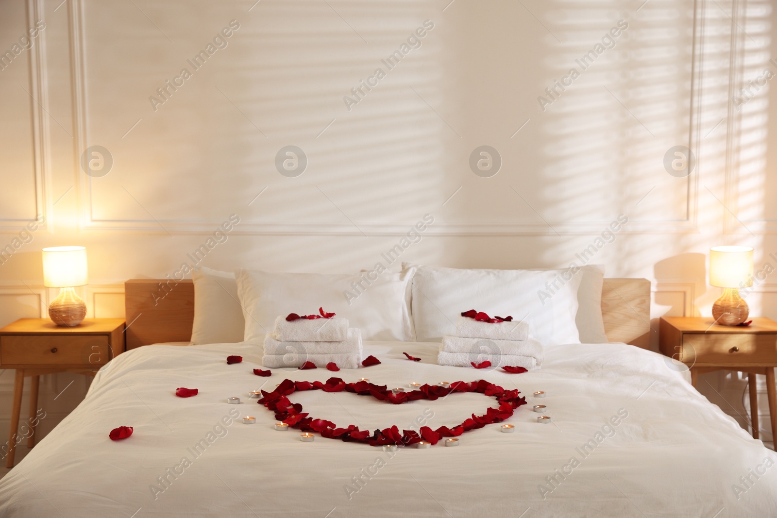 Heart made with rose petals and burning candles on bed indoors Photo of Heart made with rose petals and burning candles on bed indoors