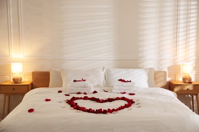 Photo of Heart made with rose petals and burning candles on bed indoors
