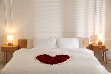Photo of Heart made with rose petals and burning candles on bed indoors