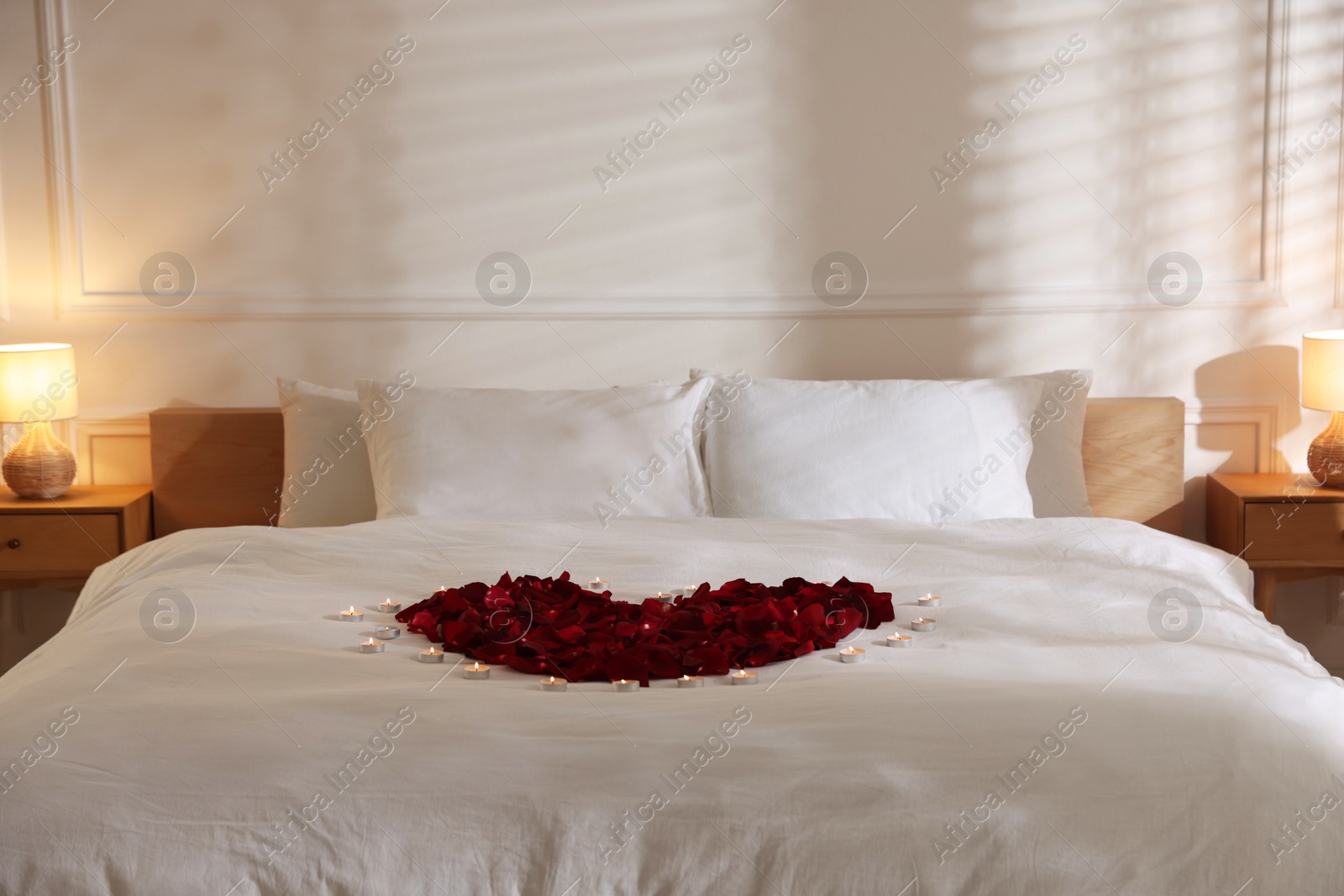 Heart made with rose petals and burning candles on bed indoors Photo of Heart made with rose petals and burning candles on bed indoors