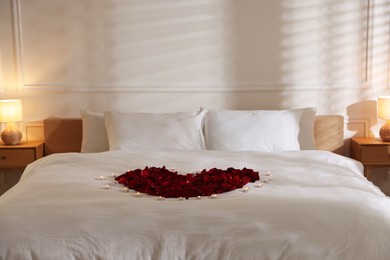 Photo of Heart made with rose petals and burning candles on bed indoors