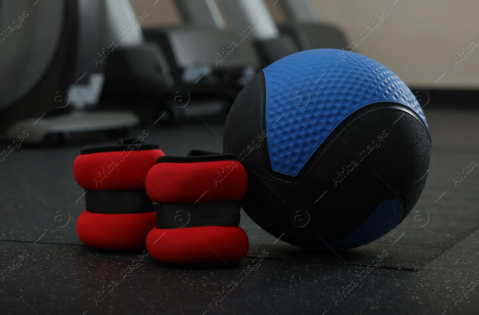 Blue medicine ball and ankle weights on floor in gym, space for text Photo of Blue medicine ball and ankle weights on floor in gym, space for text
