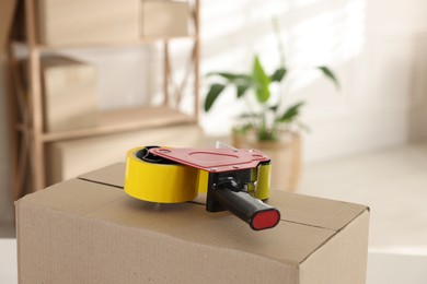 Photo of Dispenser with adhesive tape on cardboard box indoors, closeup