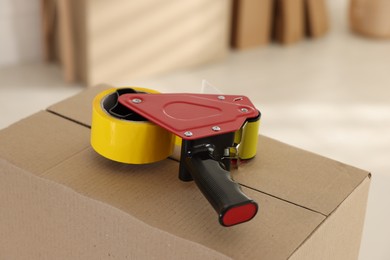 Photo of Dispenser with adhesive tape on cardboard box indoors, closeup