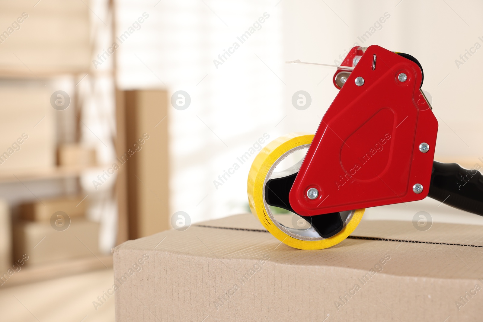 Photo of Dispenser with adhesive tape on cardboard box indoors, closeup