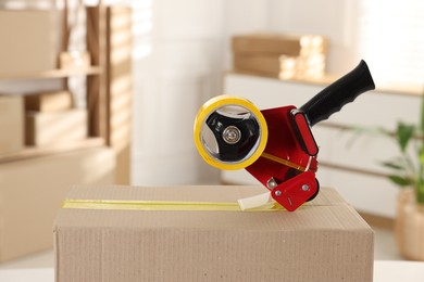 Photo of Dispenser with adhesive tape on cardboard box indoors, closeup