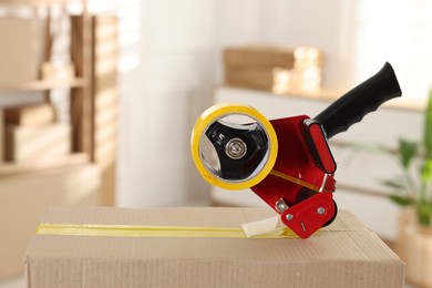 Photo of Dispenser with adhesive tape on cardboard box indoors, closeup