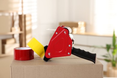 Photo of Dispenser with adhesive tape rolls on cardboard box indoors, closeup