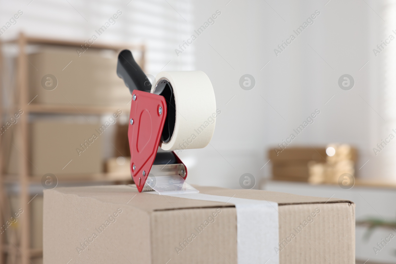 Photo of Dispenser with adhesive tape on cardboard box indoors, closeup