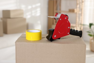 Photo of Dispenser with adhesive tape on cardboard box indoors, closeup