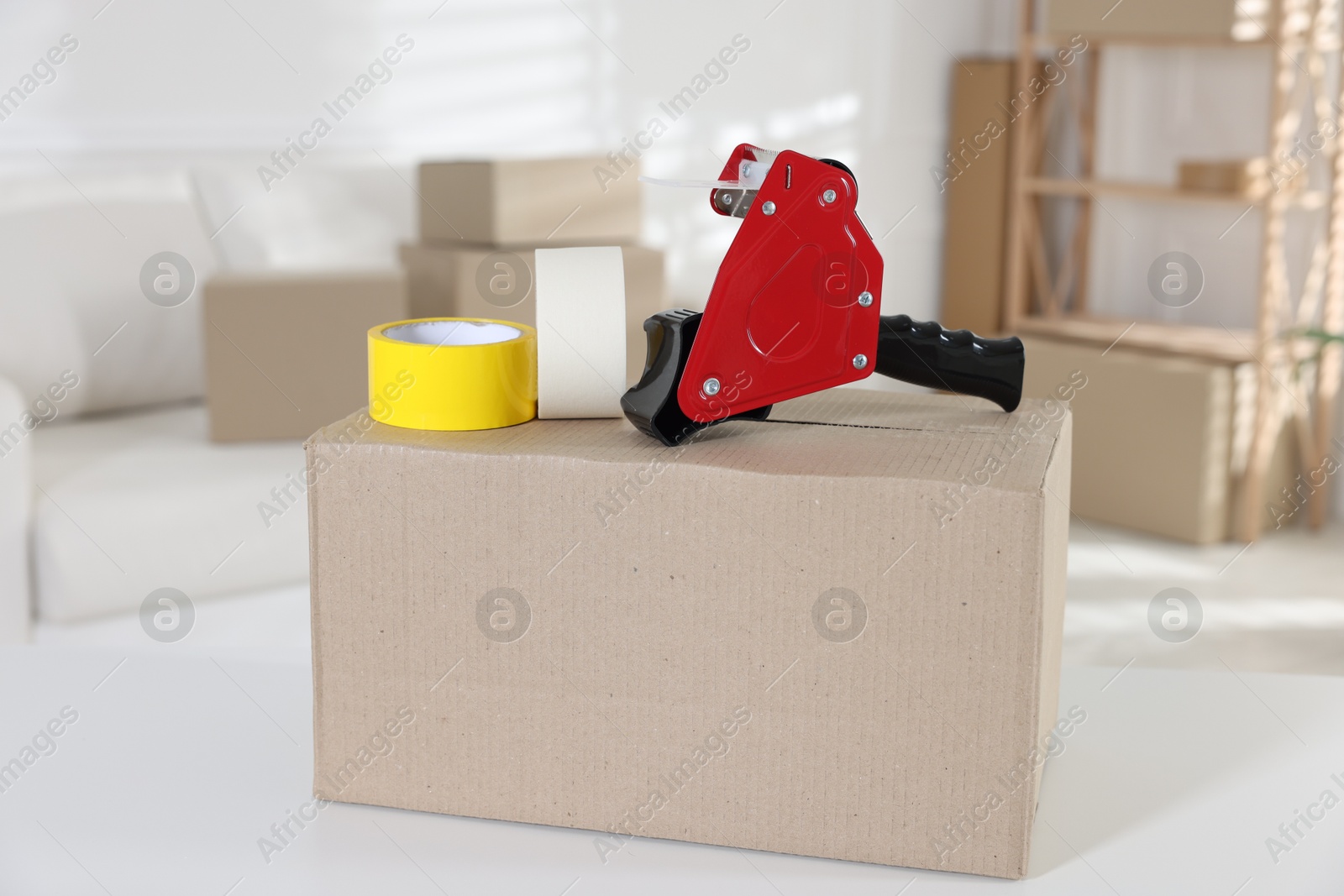 Photo of Dispenser with adhesive tape rolls and cardboard box on desk indoors
