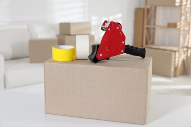 Photo of Dispenser with adhesive tape rolls and cardboard box on desk indoors
