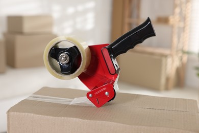 Photo of Dispenser with adhesive tape on cardboard box indoors, closeup