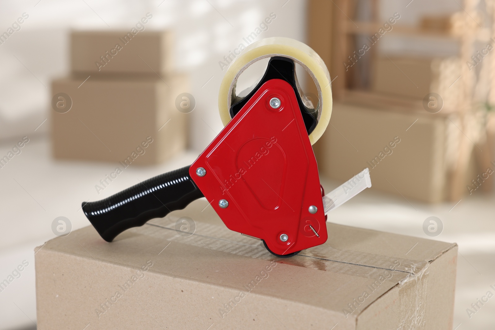 Photo of Dispenser with adhesive tape on cardboard box indoors, closeup