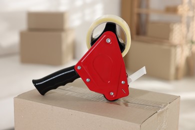 Photo of Dispenser with adhesive tape on cardboard box indoors, closeup