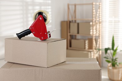 Photo of Dispenser with adhesive tape on cardboard box indoors, closeup