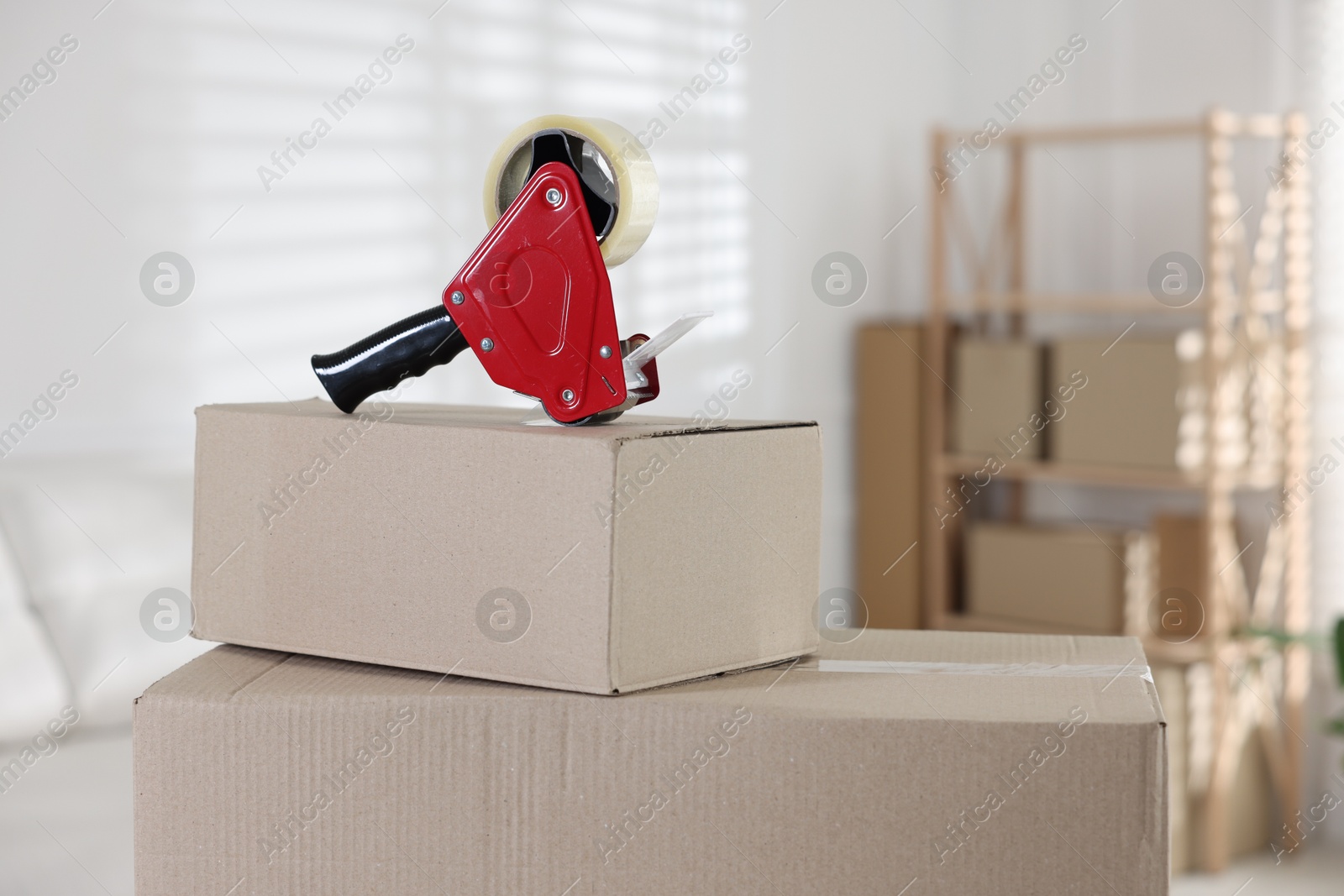 Photo of Dispenser with adhesive tape on cardboard box indoors, closeup