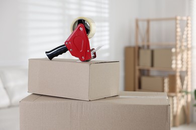 Photo of Dispenser with adhesive tape on cardboard box indoors, closeup