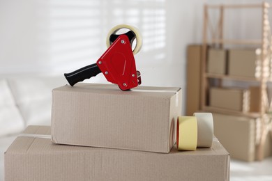 Photo of Dispenser with adhesive tape rolls on cardboard box indoors, closeup