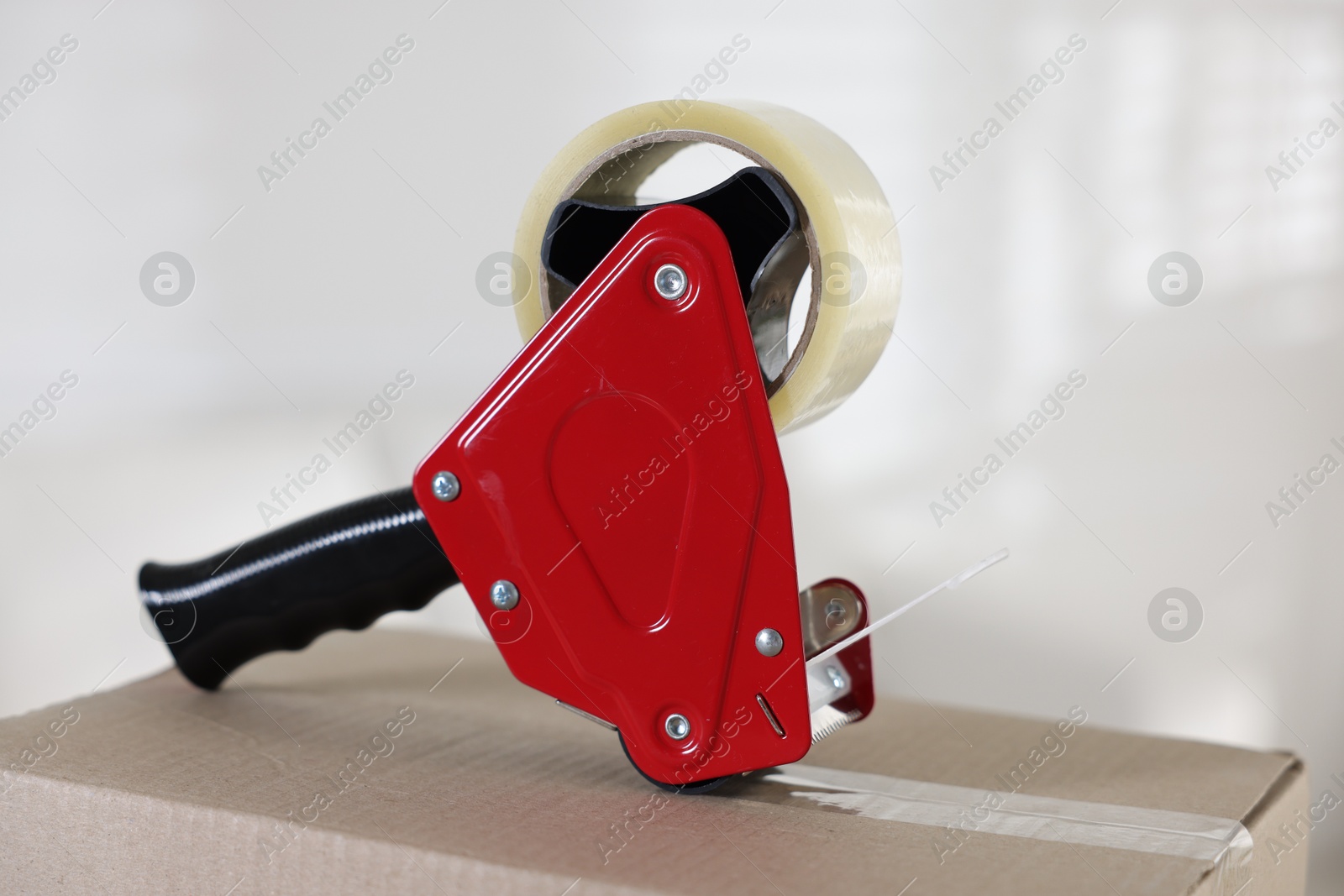 Dispenser with adhesive tape on cardboard box indoors, closeup Photo of Dispenser with adhesive tape on cardboard box indoors, closeup