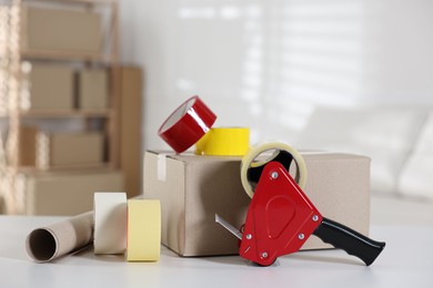 Photo of Dispenser with adhesive tape rolls and cardboard box on desk indoors