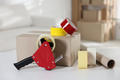 Photo of Dispenser with adhesive tape rolls and cardboard box on desk indoors