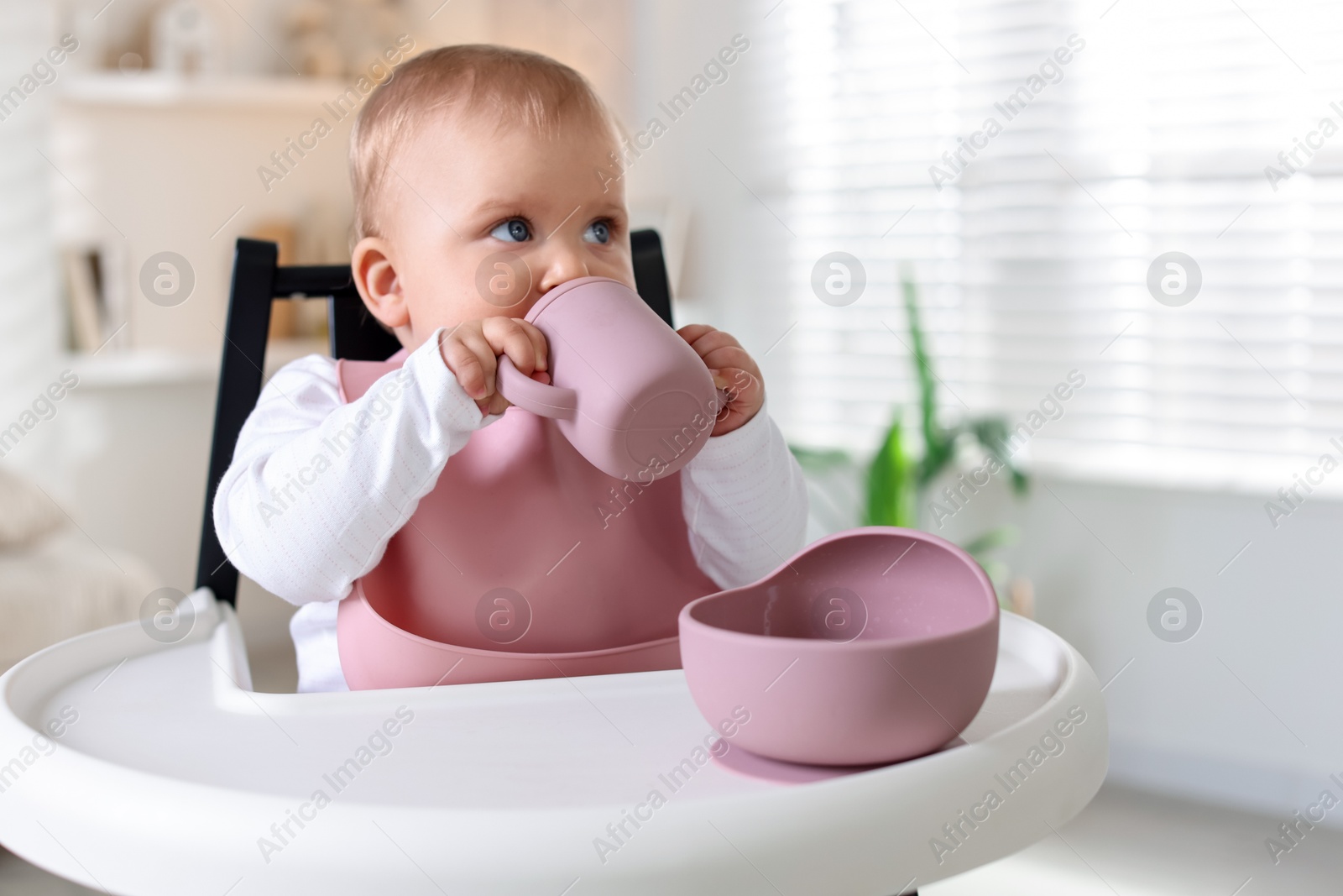 Cute little baby with bottle on feeding chair at home. Space for text Photo of Cute little baby with bottle on feeding chair at home. Space for text