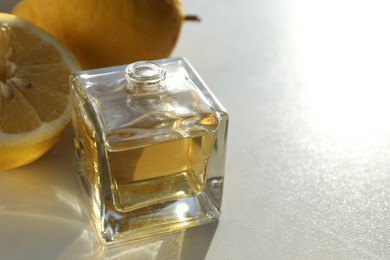 Photo of Perfume bottle with aromatic oil and lemons on light background, closeup. Space for text