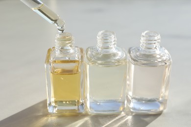 Photo of Taking aromatic oil from perfume bottle with dropper on light background, closeup