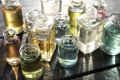 Photo of Perfume bottles with aromatic oils on black wooden background, closeup