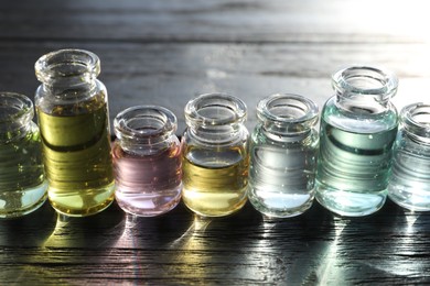 Photo of Perfume bottles with aromatic oils on black wooden background, closeup