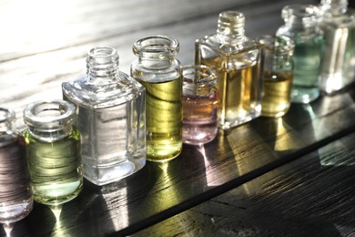 Photo of Perfume bottles with aromatic oils on black wooden background, closeup