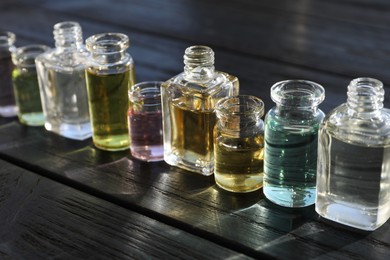Photo of Perfume bottles with aromatic oils on black wooden background, closeup
