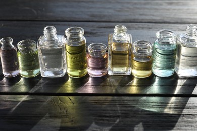 Photo of Perfume bottles with aromatic oils on black wooden background, closeup