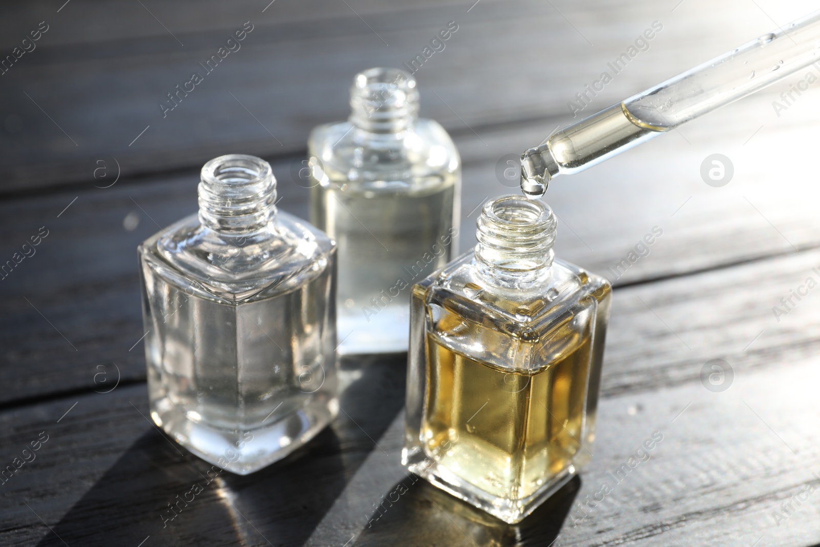 Taking aromatic oil from perfume bottle with dropper on black wooden background, closeup Photo of Taking aromatic oil from perfume bottle with dropper on black wooden background, closeup
