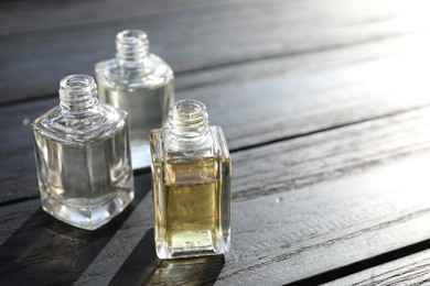 Photo of Perfume bottles with aromatic oils on black wooden background, closeup. Space for text