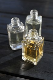 Photo of Perfume bottles with aromatic oils on black wooden background, closeup
