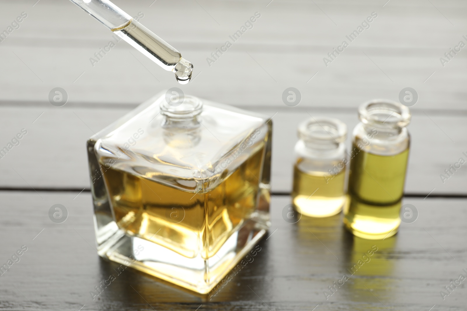 Taking aromatic oil from perfume bottle with dropper on black wooden background, closeup Photo of Taking aromatic oil from perfume bottle with dropper on black wooden background, closeup