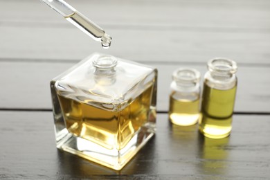 Photo of Taking aromatic oil from perfume bottle with dropper on black wooden background, closeup