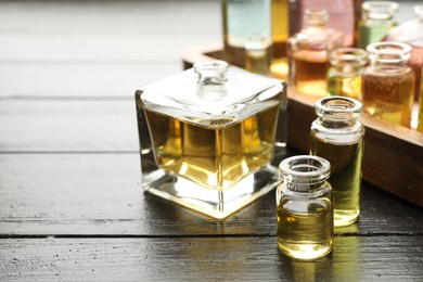 Photo of Perfume bottles with aromatic oils on black wooden background, closeup