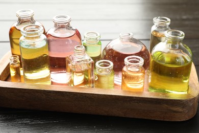Photo of Perfume bottles with aromatic oils on black wooden background, closeup