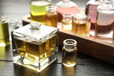 Photo of Perfume bottles with aromatic oils on black wooden background, closeup