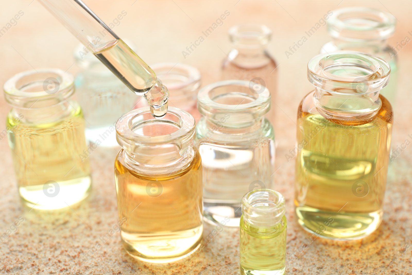 Photo of Taking aromatic oil from perfume bottle with dropper on beige textured background, closeup