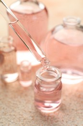 Photo of Taking aromatic oil from perfume bottle with dropper on beige textured background, closeup